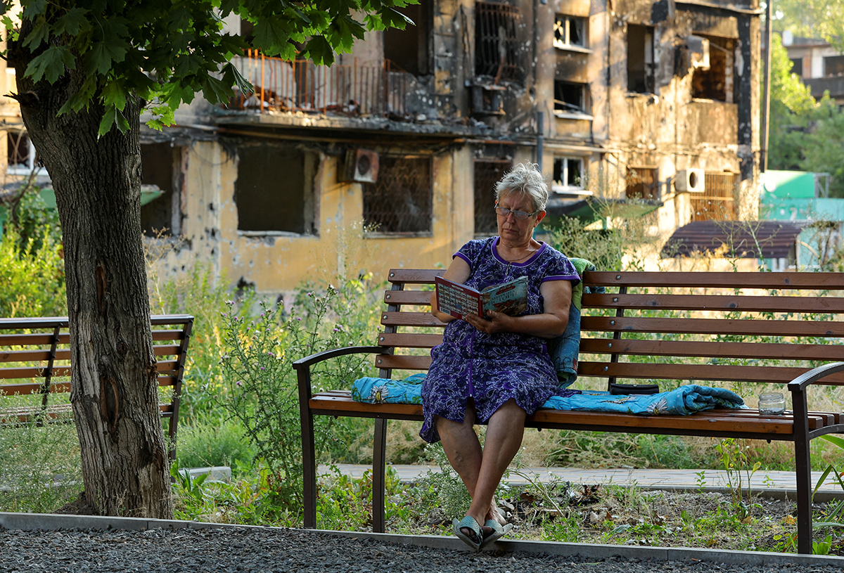 Пожилая женщина читает книгу во дворе дома. Мариуполь, Украина, 15 июля 2022 года. Фото: Reuters